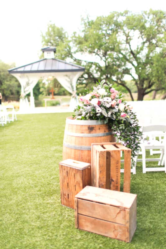 Wood barrels and crates and flowers used as wedding aisle decor.