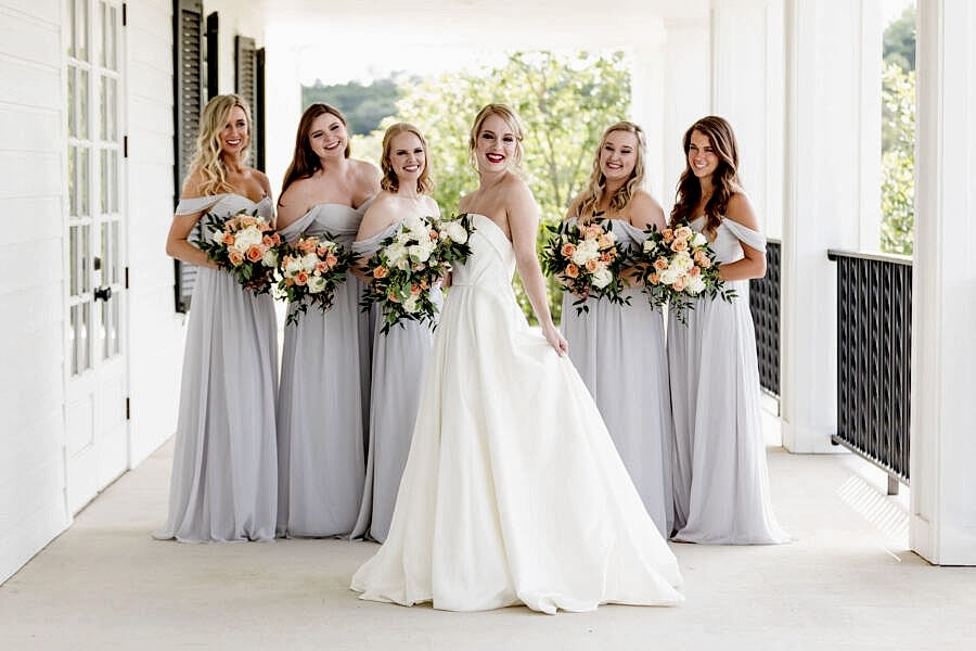 The bride and her bridesmaids smile for photos on the porch.