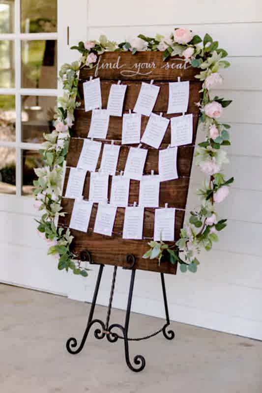 A wooden sign with a simple floral wreath lists the seating assignments for dinner.