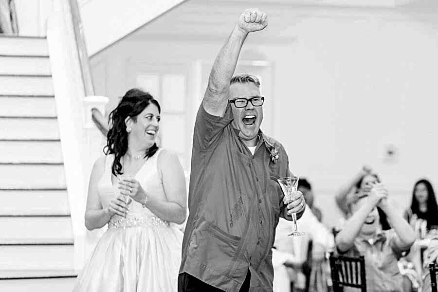 Black and white photo and bride and groom cheering during their reception