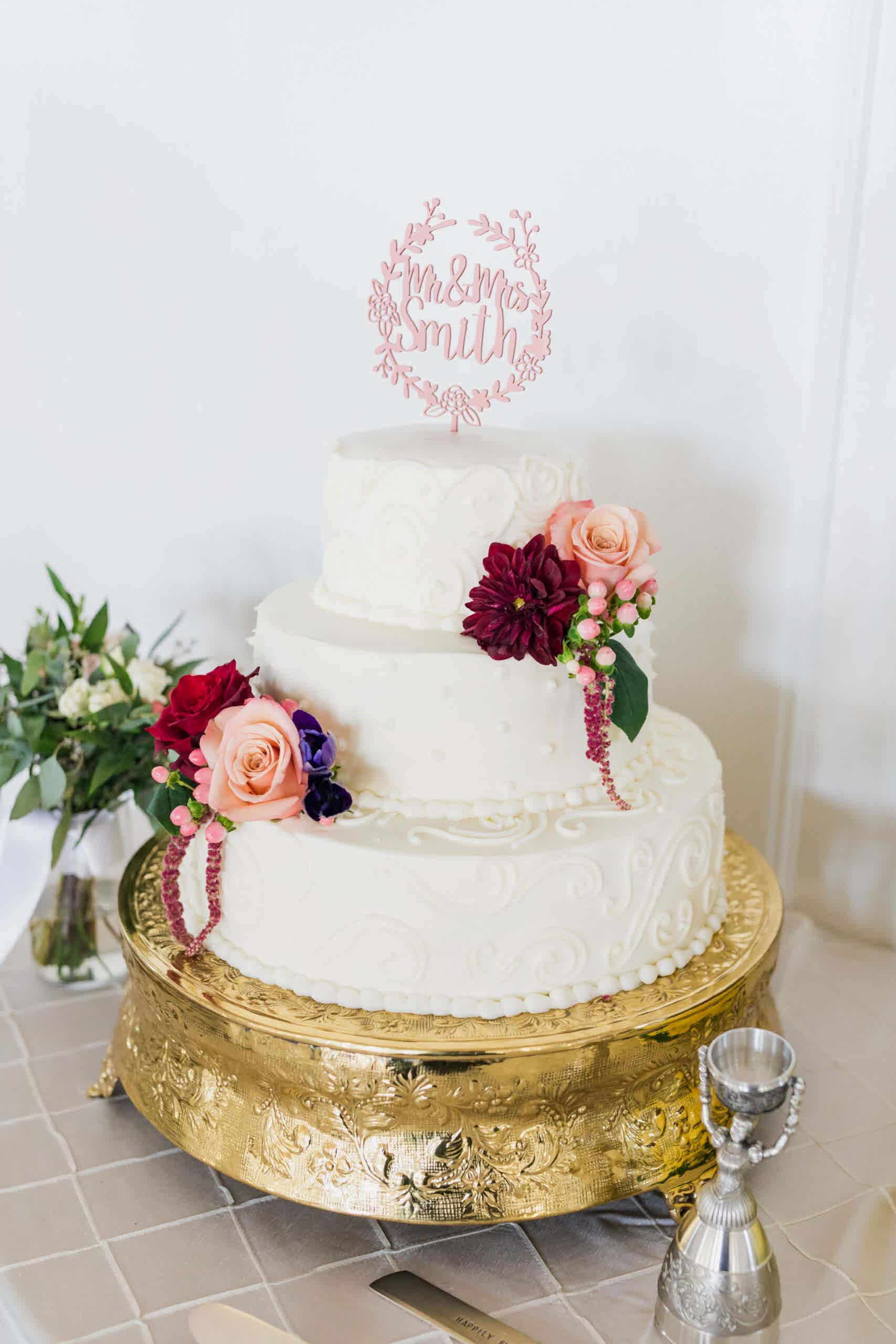 White wedding cake with pink and burgundy flowers. 