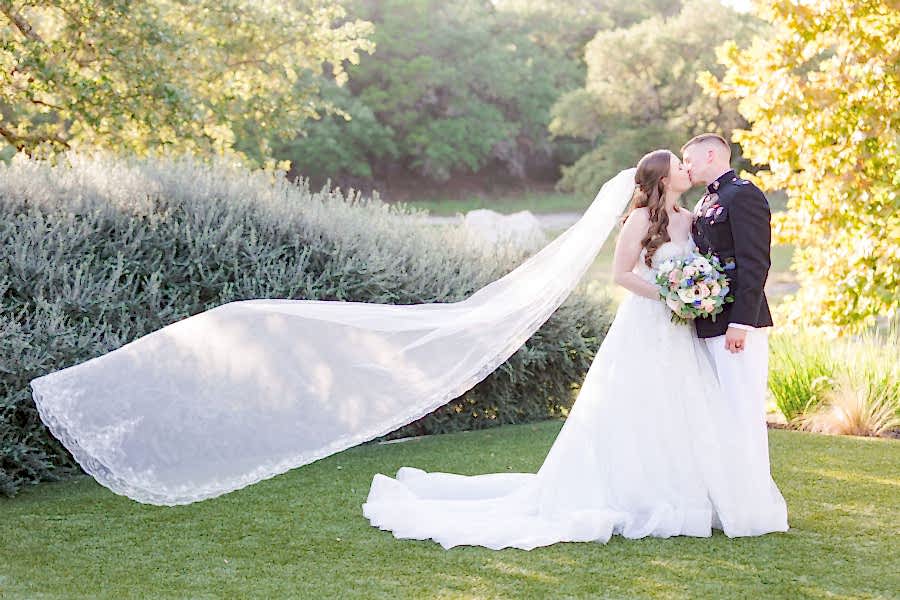 Bride and groom kiss with bride's veil flowing behind her.