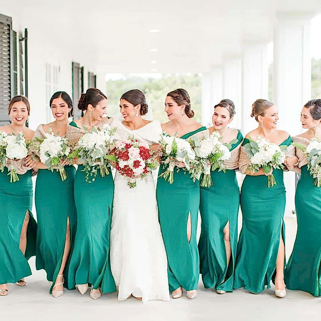 Bride and bridesmaids in green dresses and fur wraps with red and white flowers for a Christmas themed wedding.