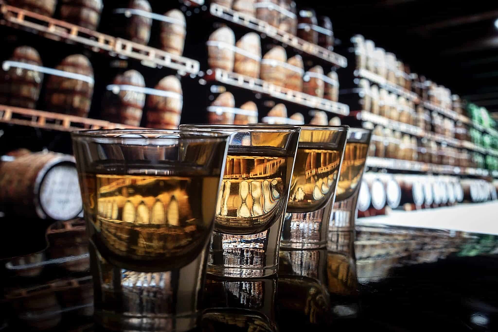 close up of whiskey glasses on bar with barrels in background